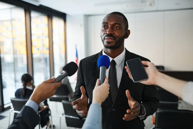Confident businessman answering questions from the media during a press conference indoors. Comparing corporate communications pricing mechanics on the same record