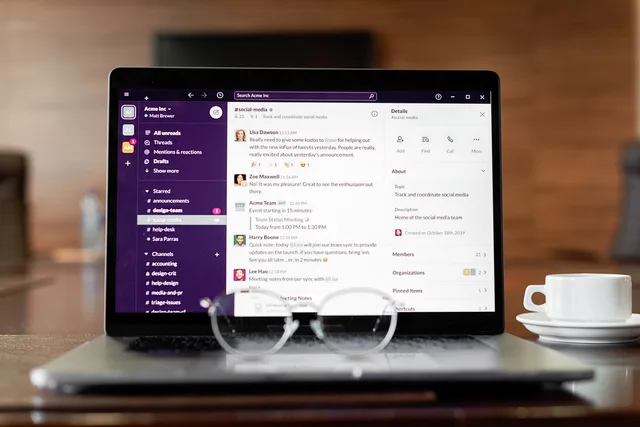 Laptop displaying a messaging app, with eyeglasses and coffee cup on a wooden table. Teams or Slack for corporate communications? What the records settle and what they cannot