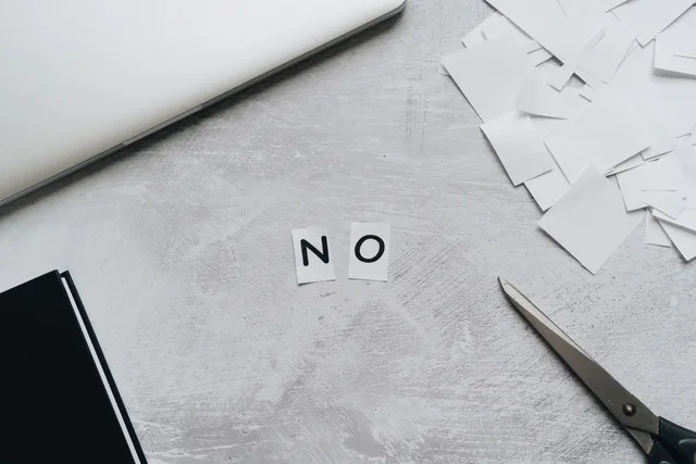 Top view of scattered paper squares, laptop, and scissors forming the word 'NO', implying rejection or denial. Close-out checklist for a corporate communications release