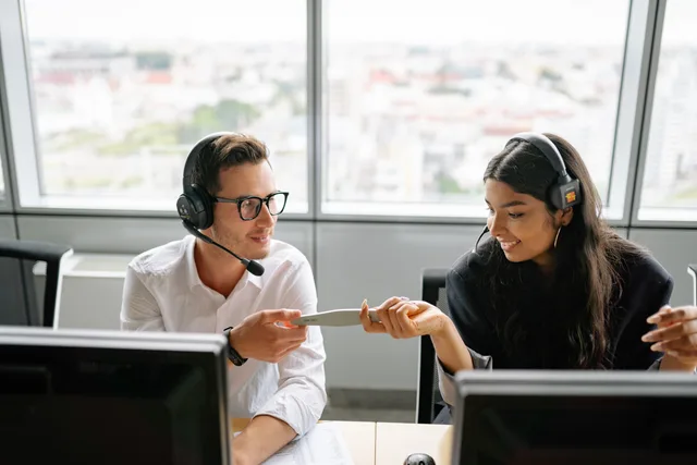 Two call center agents sharing a document while communicating with clients, fostering teamwork. An evidence-led corporate communications strategy for a single decision
